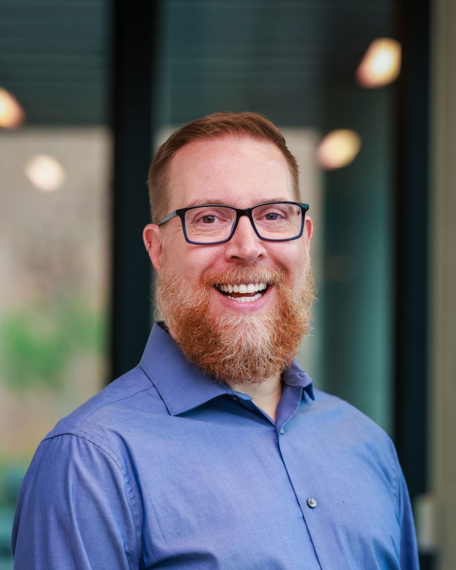 Professional portrait of Andrew Bertke in a blue button-down shirt and dark-rimmed glasses